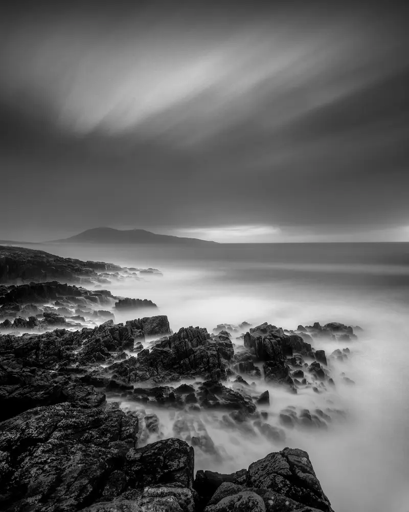 a rocky landscape with a body of water in the distance. landscape cloud black and white sky fog outdoor nature water monochrome seascape sea ocean beach clouds rock coast