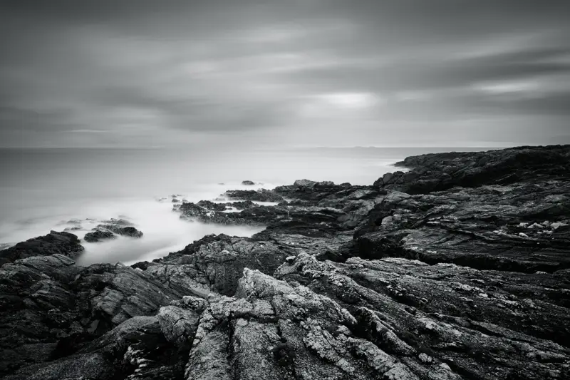 a person standing on a rocky hill. sky outdoor landscape mountain black and white cloud rock sea fog nature seascape ocean coast rocky monochrome water beach hill
