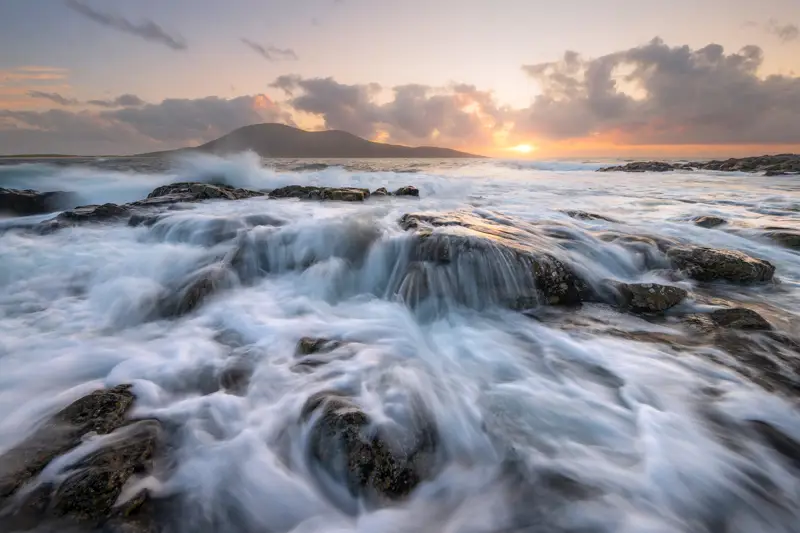 a body of water with rocks and waves crashing on it. water outdoor sky nature cloud landscape sunrise body of water seascape tide wind wave water resources sea horizon ocean clouds beach rock sunset coast cloudy wave
