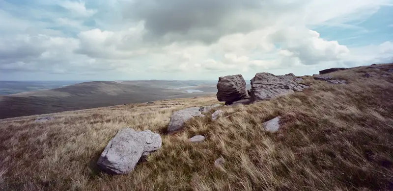 Rocks high on moors. a field with a mountain in the background. sky outdoor grass landscape cloud nature field mountain desert rock grassy